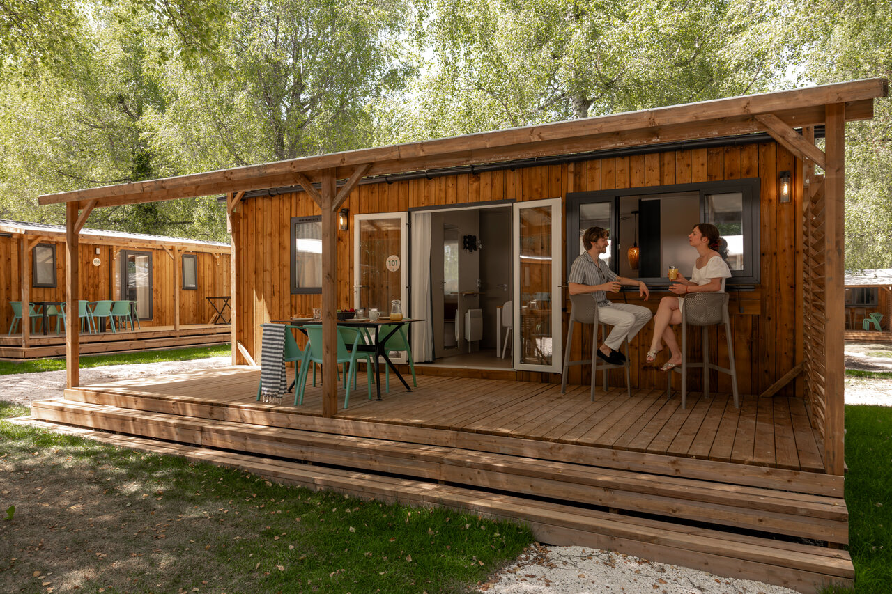 Wooden mobile home, couple on terrace, outdoor bar, camping CLICOCHIC Aloua.