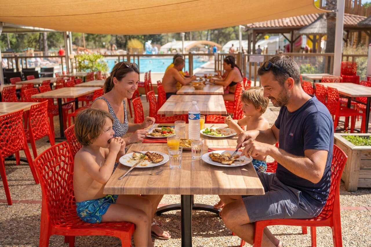 Family having lunch at outdoor restaurant near swimming pool at CAPFUN Arbois du Castellet campsite in LE CASTELLET (83).