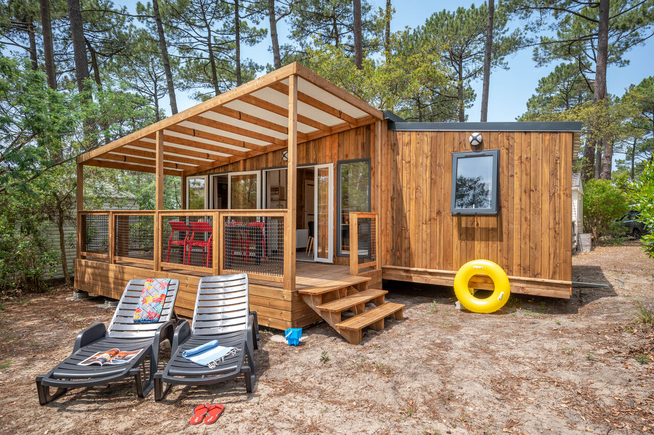 Wooden mobile home, covered terrace, sun loungers at LIBRANOO Naturiste Arnaoutchot campsite, Landes.