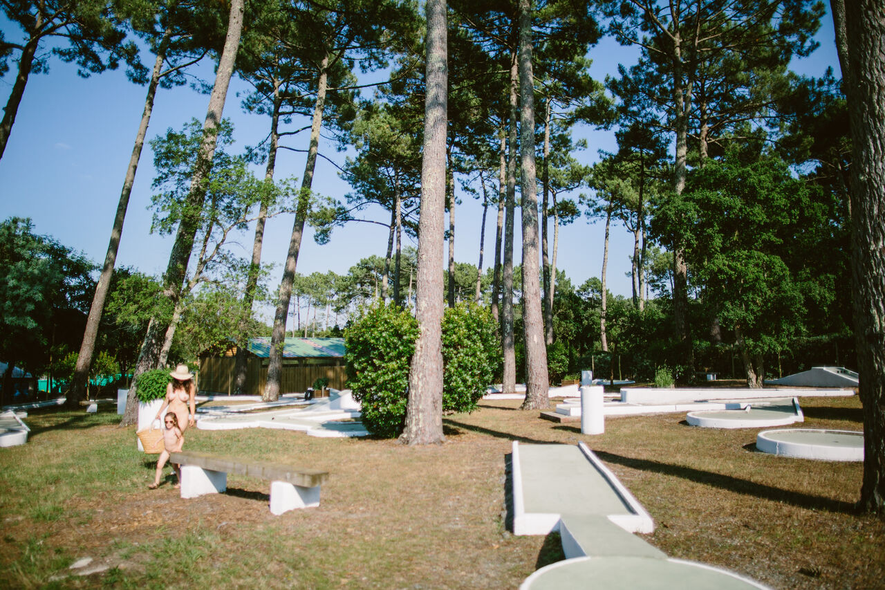Shaded mini-golf course under pine trees with family at LIBRANOO Naturiste Arnaoutchot campsite in Veille-Saint-Girons, Landes, France.