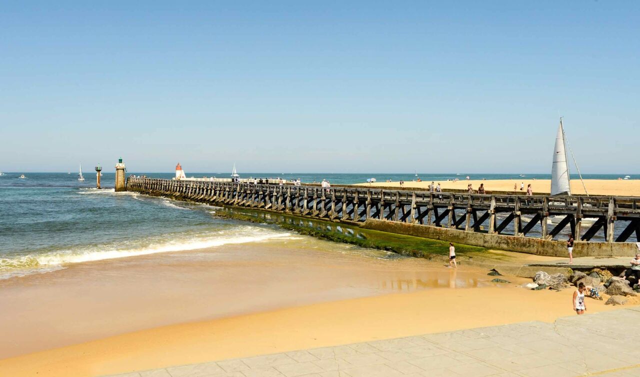 Sandy beach, wooden pier, sailboats at LIBRANOO Naturiste Arnaoutchot campsite.