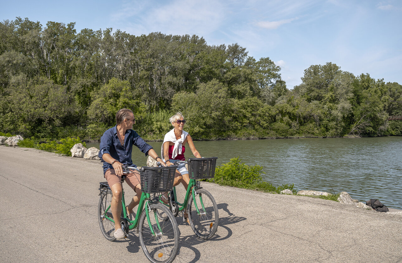 Couple cycling along a river, lush nature at CLICOCHIC Art de Vivre campsite in Ch�teauneuf du Pape (84).