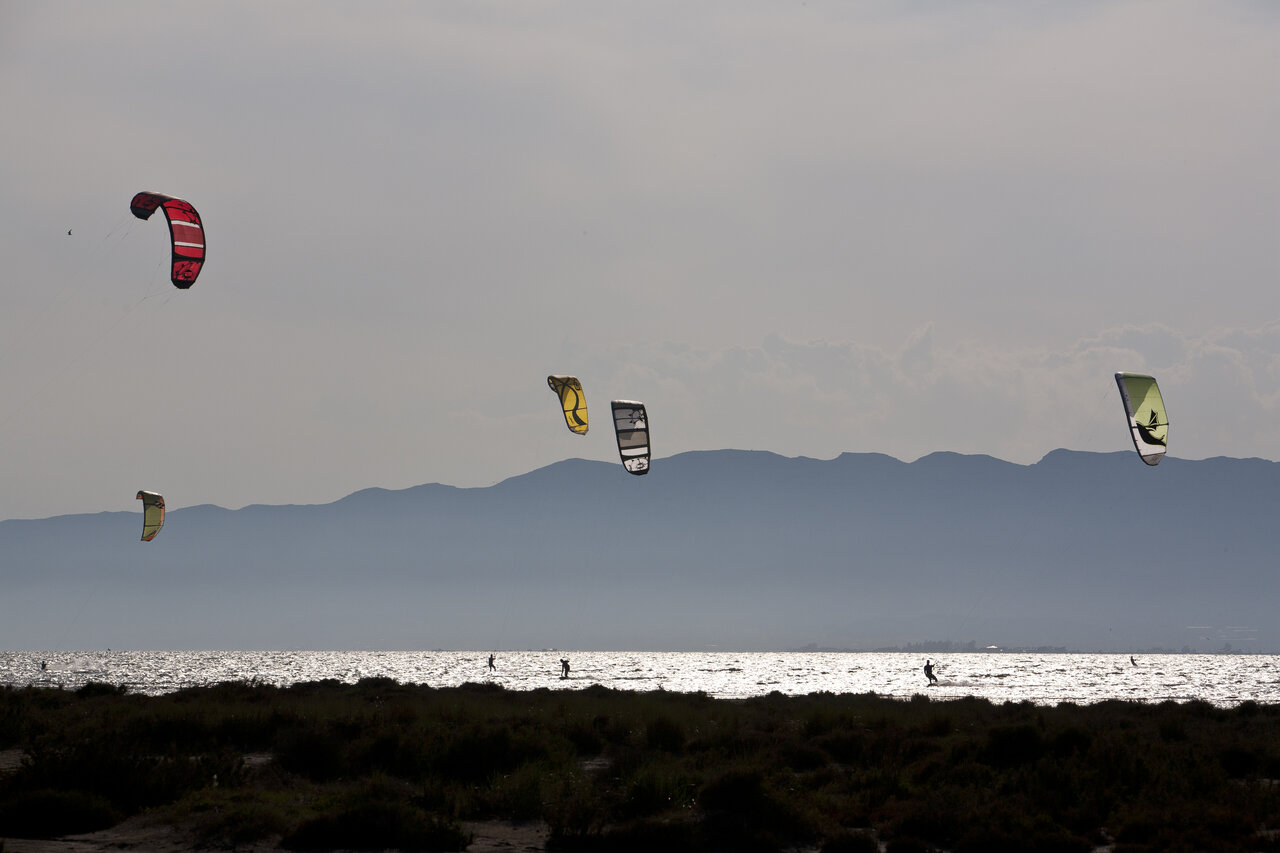 Kitesurfers on sparkling water with mountains at CAPFUN Aube campsite in Deltebre, Tarragona.