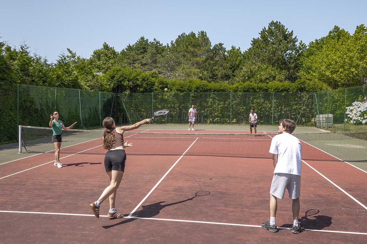 Tennis players on the outdoor court at CLICOCHIC Baie de Douarnenez campsite.