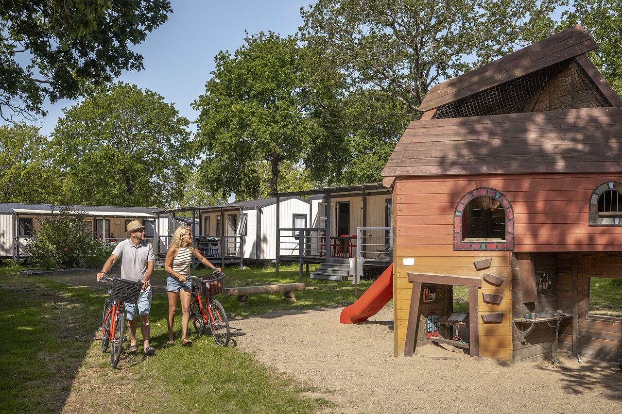Mobile homes, playground, couple on bikes at CLICOCHIC campsite in Poullan-sur-Mer.