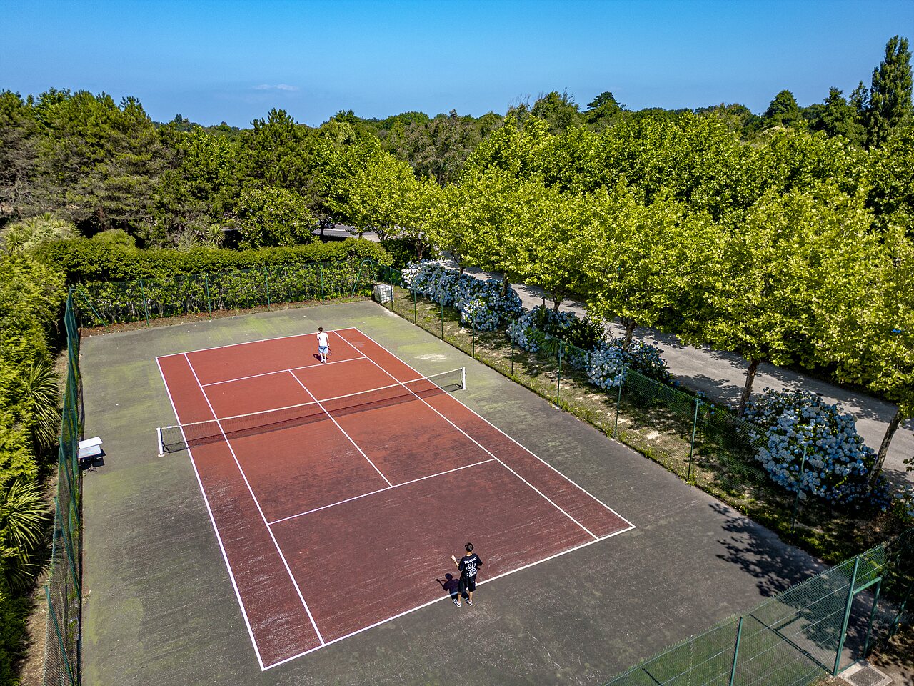 Outdoor tennis court with players at CLICOCHIC Baie de Douarnenez campsite (29).