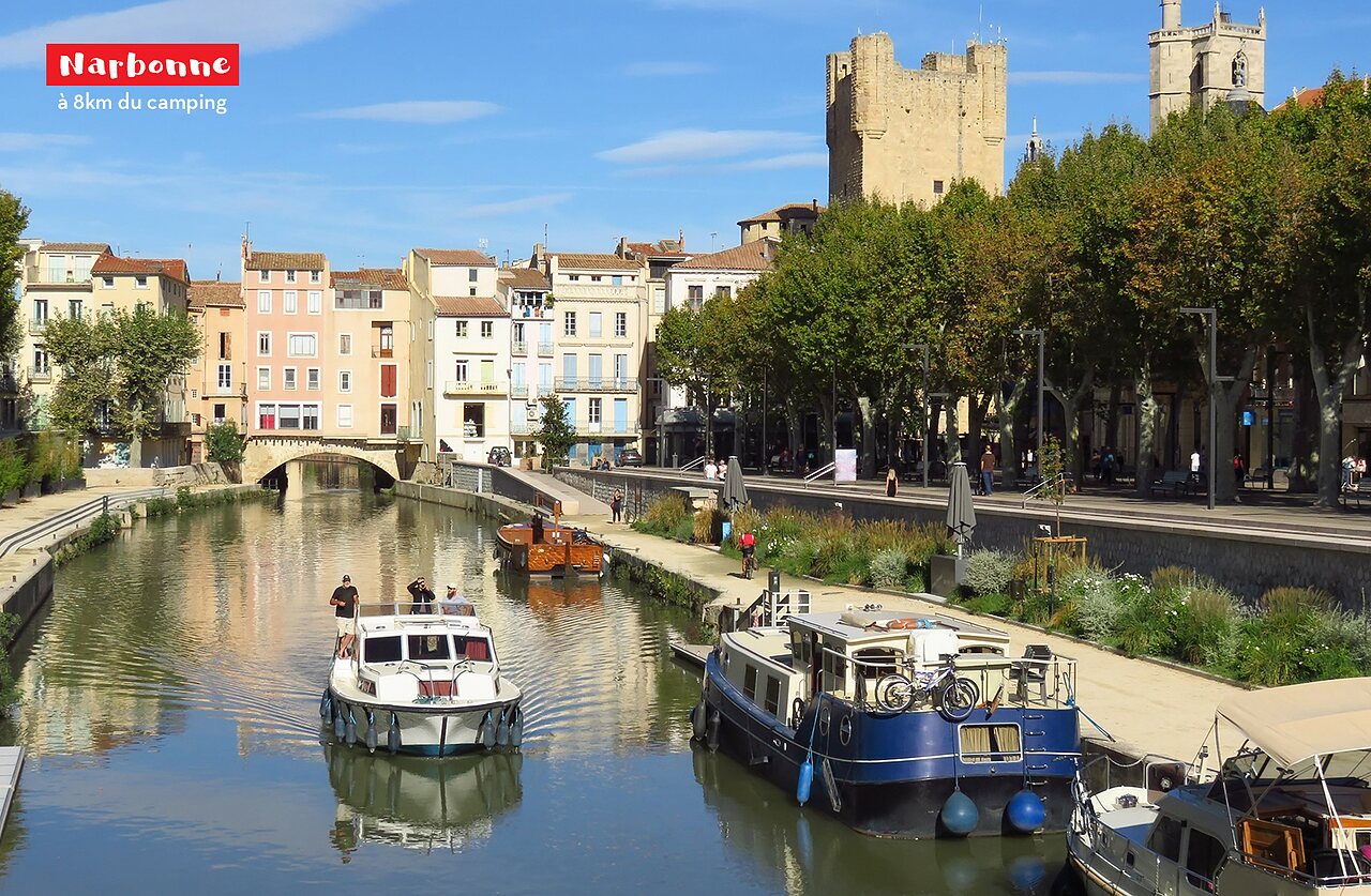 Canal de la Robine with boats, historic buildings and tower in Narbonne.