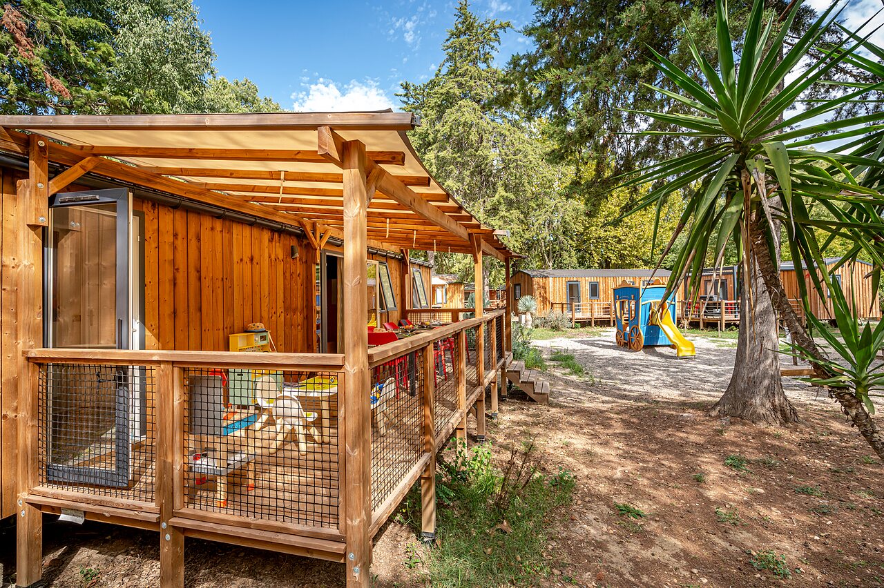 Wooden mobile home with covered terrace and playground at CAPFUN Bastide campsite in N�mes (30).