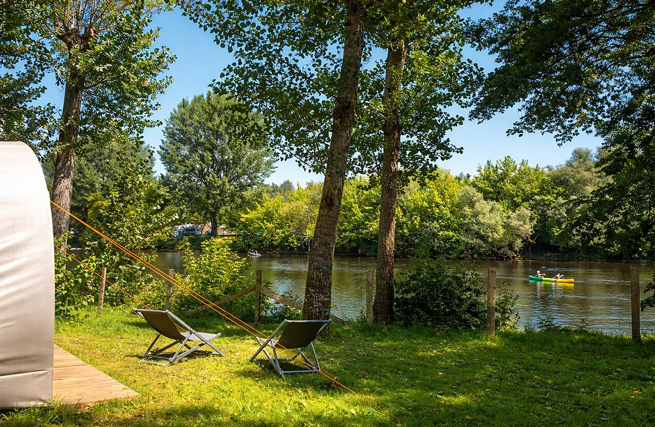 Kayak on the river and lounge chairs at CLICOCHIC Beau Rivage campsite in LA ROQUE-GAGEAC.