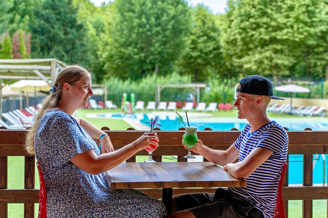Couple enjoying cocktails at the bar, pool view, at camping CLICOCHIC Beau Rivage in LA ROQUE-GAGEAC (24).