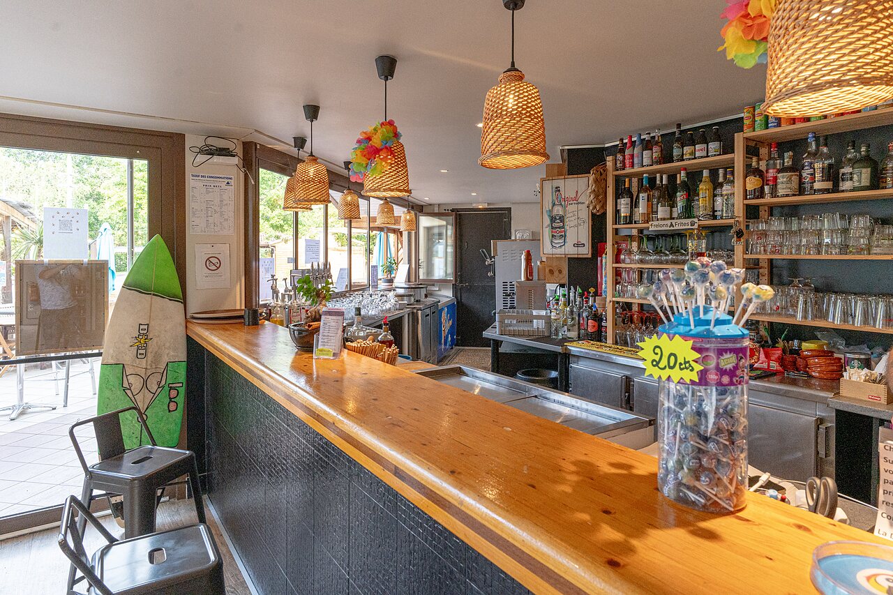 Indoor bar with wooden counter, drinks and surf decoration at CLICOCHIC Bimbo campsite in BISCARROSSE (40)