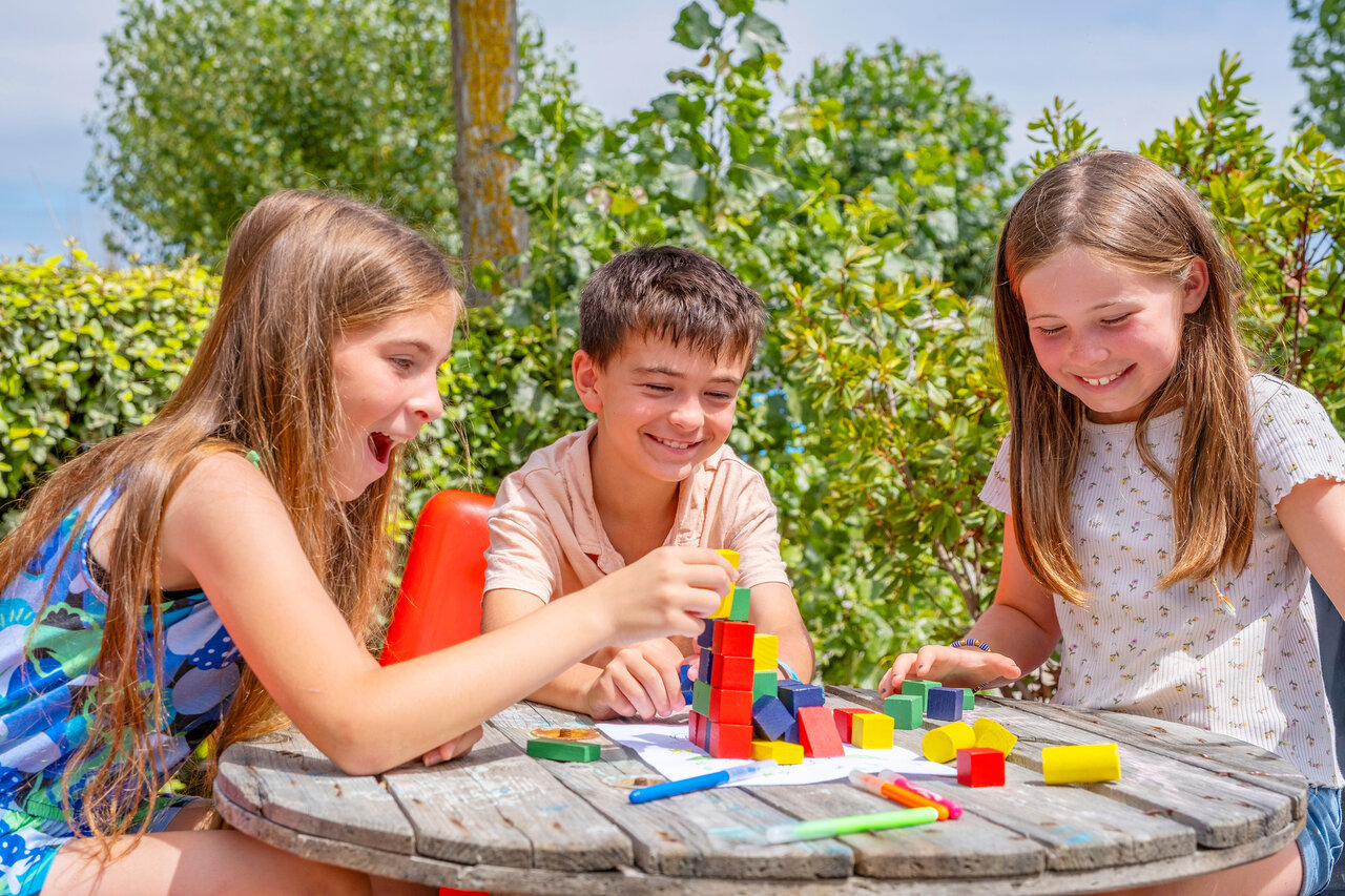 Smiling children playing with colorful building blocks at VAGUES OCEANES Bois Joly campsite.