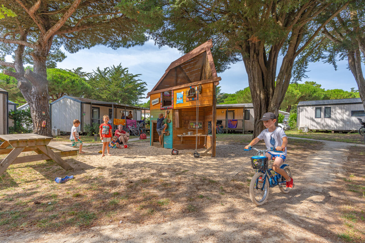 Playground with wooden playhouse, children and mobile homes at CAPFUN Bonne Etoile campsite in BOIS PLAGE EN RE (17).