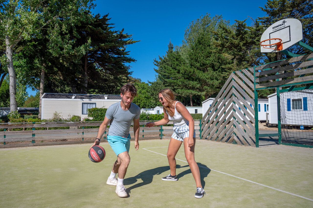 Couple playing basketball on multi-sport court at CLICOCHIC Cabanes d'Ol�ron campsite.