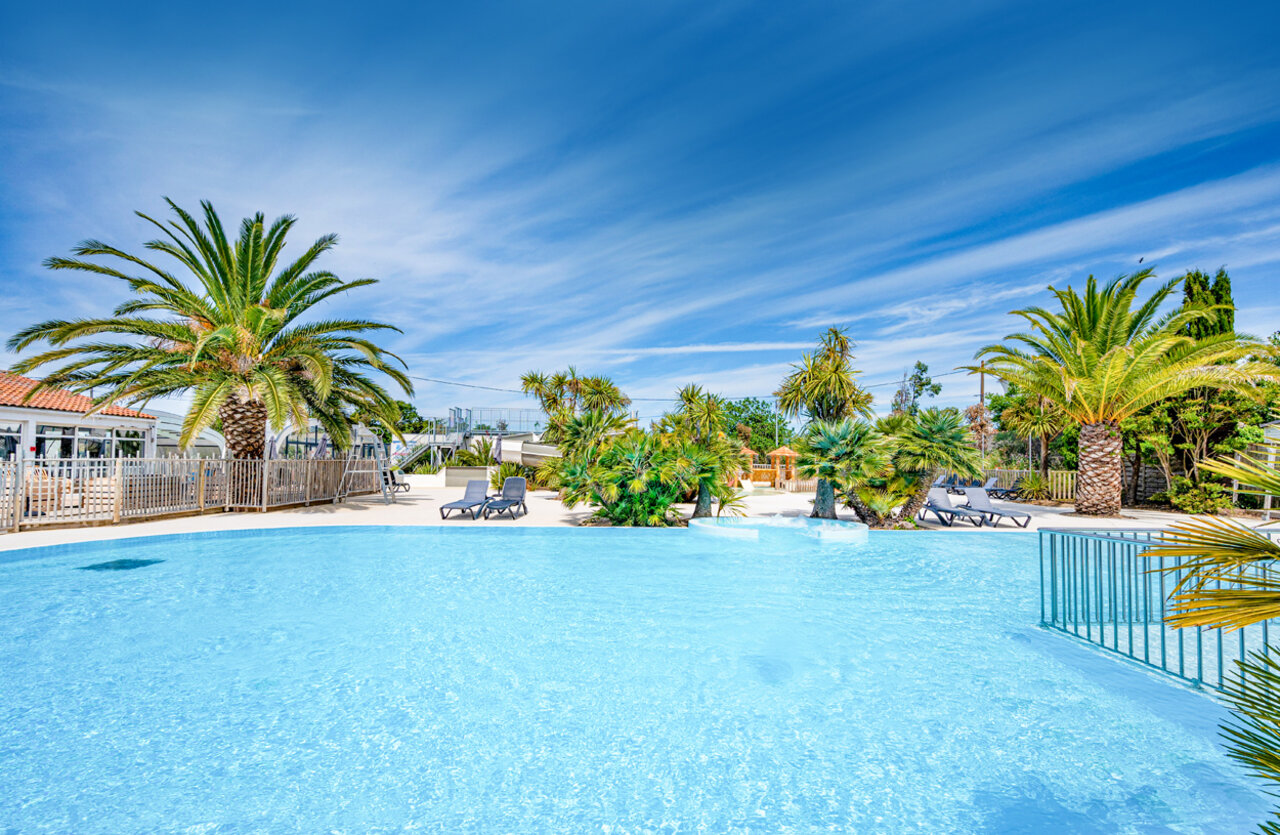 Large outdoor swimming pool, water slides and palm trees at CLICOCHIC Cabanes d Ol�ron campsite in ST GEORGES D'OLERON (17).