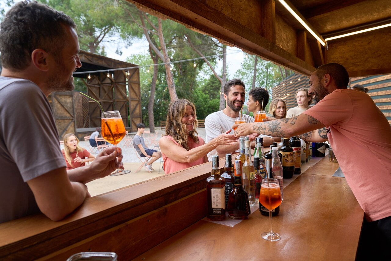 Lively outdoor bar with guests and bartender at CAPFUN Campo dei Fiori campsite in Rosignano Marittimo (57).