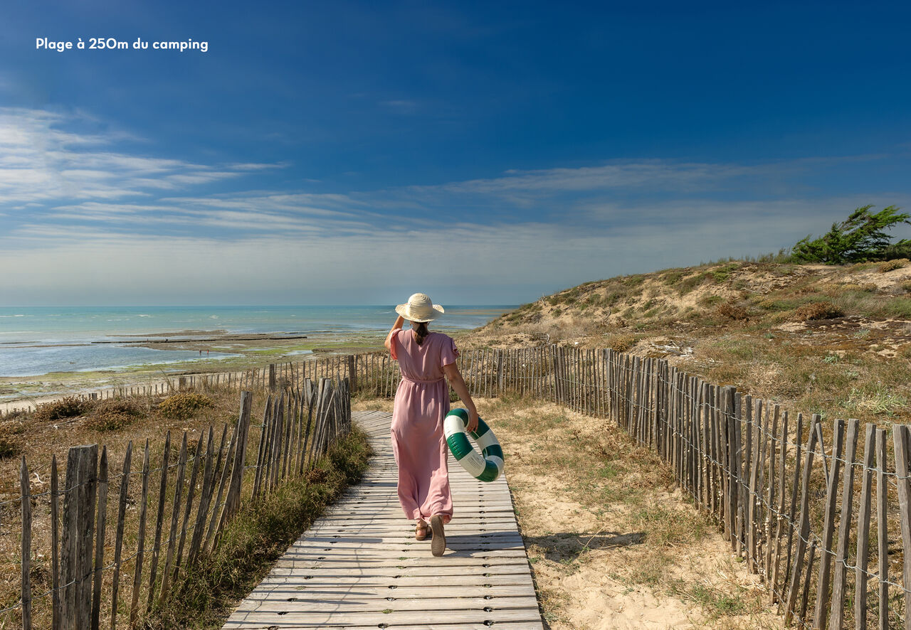 Woman walking on wooden boardwalk towards the beach at CLICOCHIC Camp du Soleil campsite in Ars-en-R� (17).
