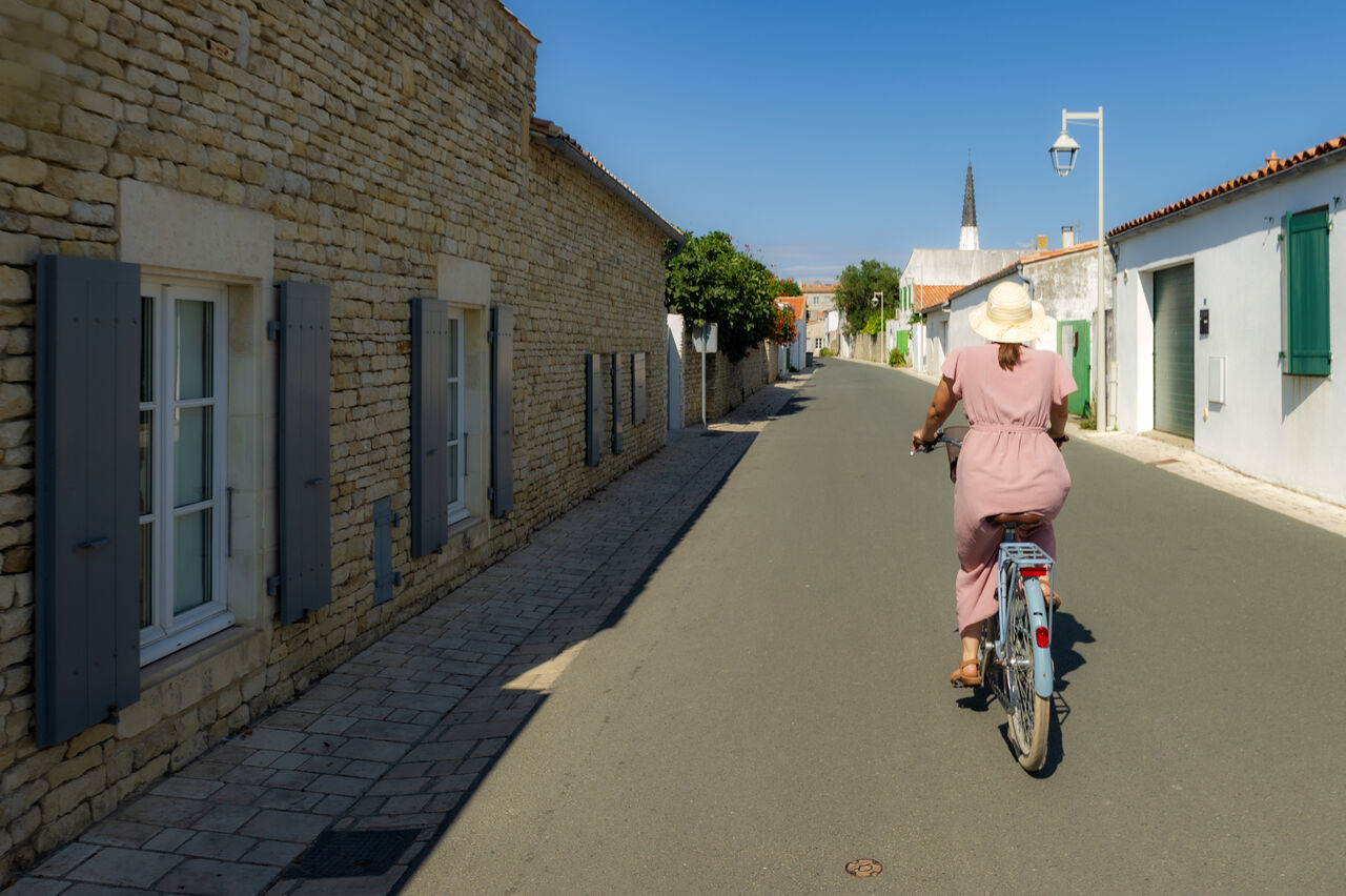 Woman cycling through charming cobbled streets of Ars-en-R�, �le de R�.