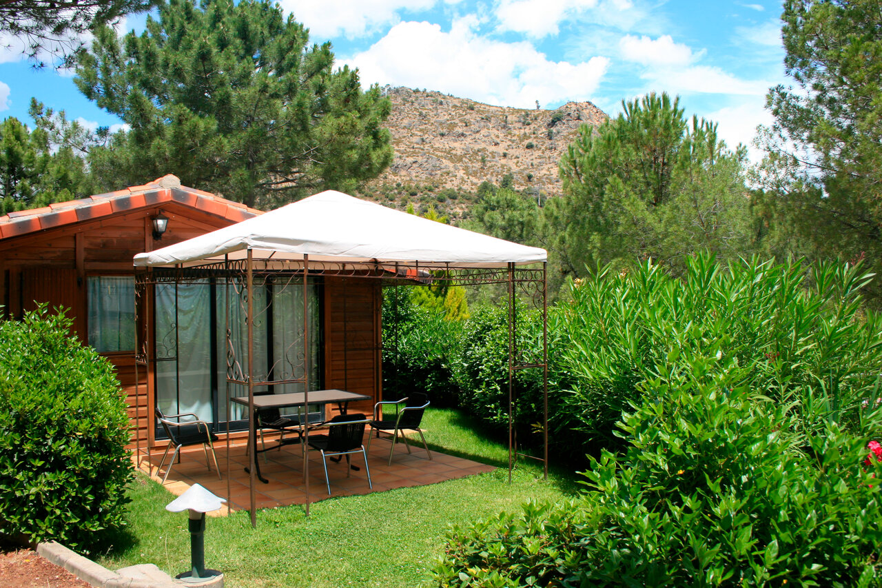 Wooden chalet, shaded terrace and greenery at CAPFUN El Canto La Gallina campsite in Valdemaqueda (Madrid).