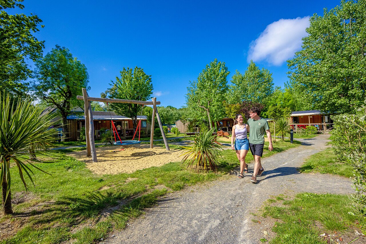 Playground with swing, couple walking, Mobil-homes at CAPFUN Cenic campsite in PENESTIN (56).