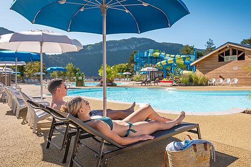Outdoor pool, water slides and couple on chairs at CLICOCHIC Chancia campsite (01).