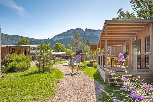 Wooden mobile homes with terraces and couple walking at CLICOCHIC Chancia campsite in Chancia (01).