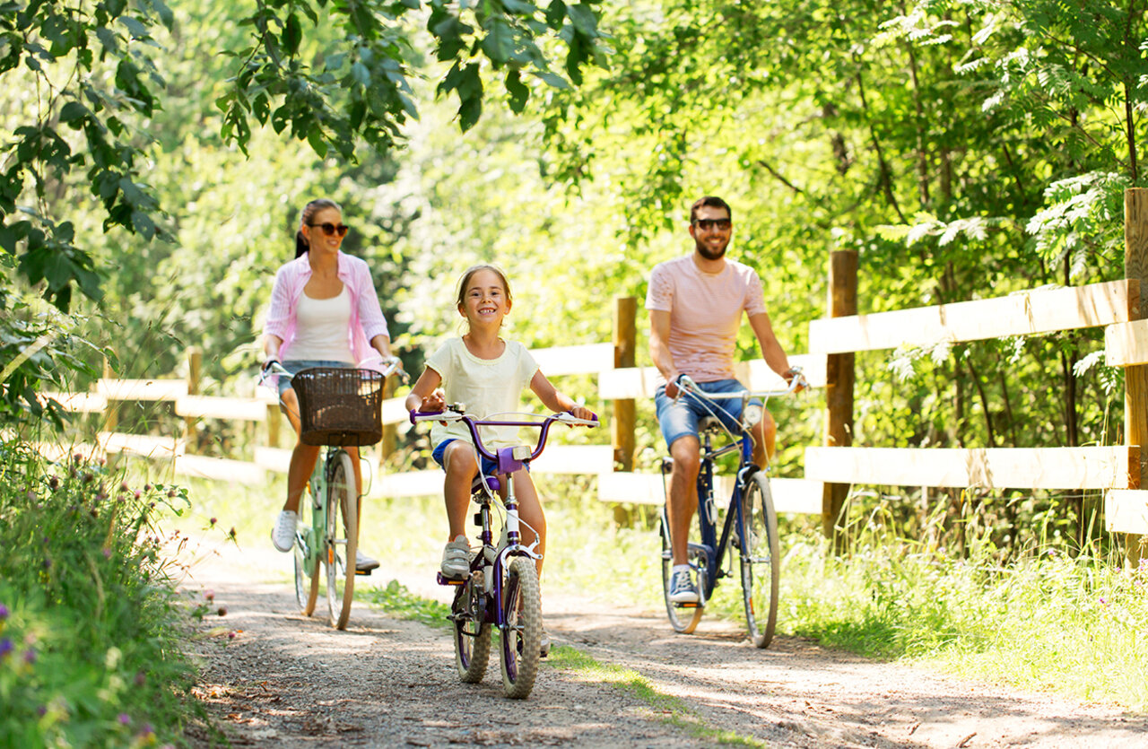 Family cycling on wooded path at VAGUES OCEANES Domaine les Charmilles campsite.