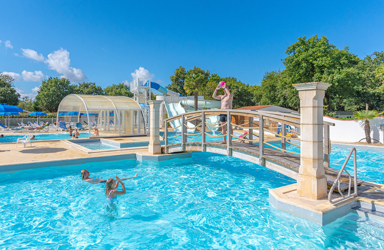 Outdoor swimming pool, water slides and decorative bridge at VAGUES OCEANES Domaine les Charmilles campsite in Saint-Laurent-de-la-Pr�e (17).