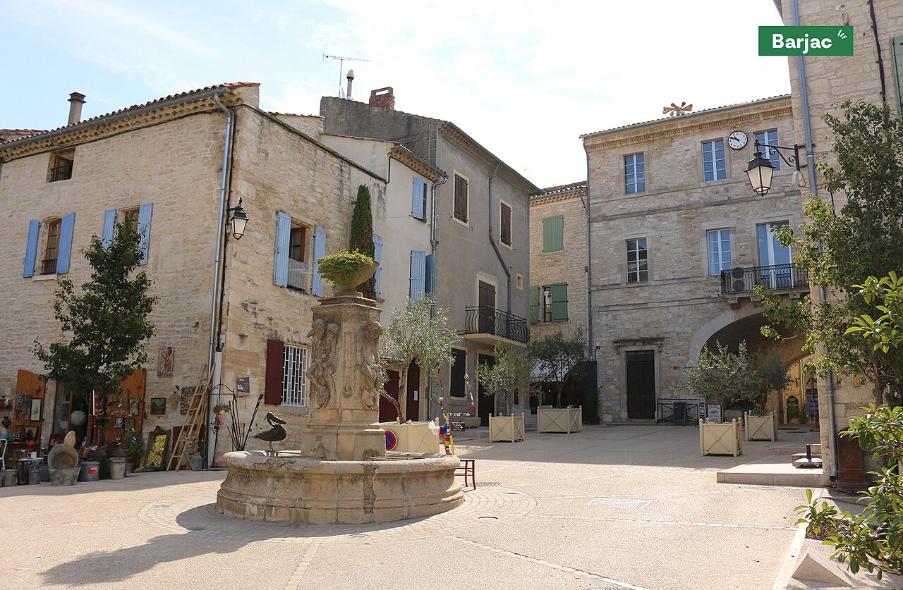 Barjac village square with fountain and stone buildings, a place to visit.