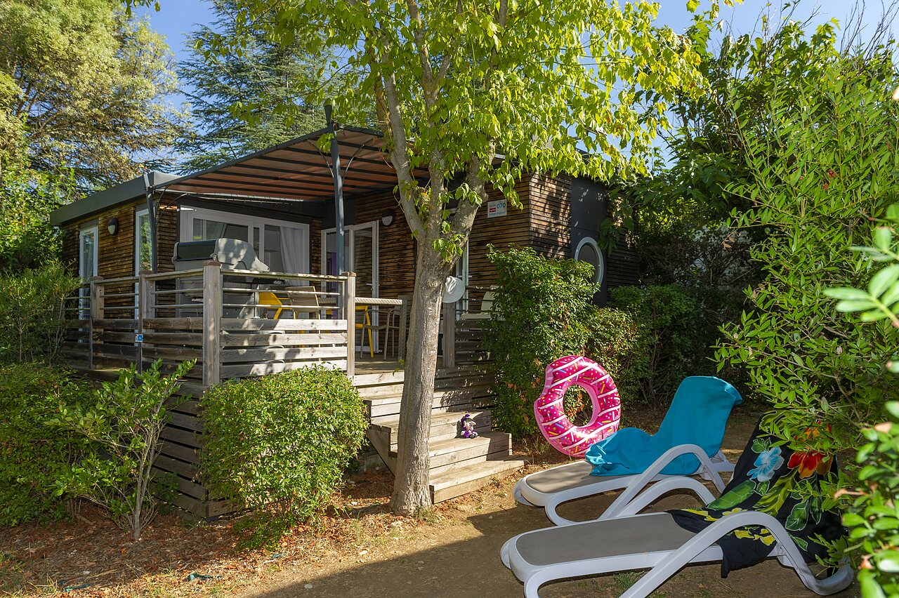 Wooden mobile home, terrace, sun loungers at camping CLICOCHIC Ch�teau de Boisson in All�gre-les-Fumades (30).