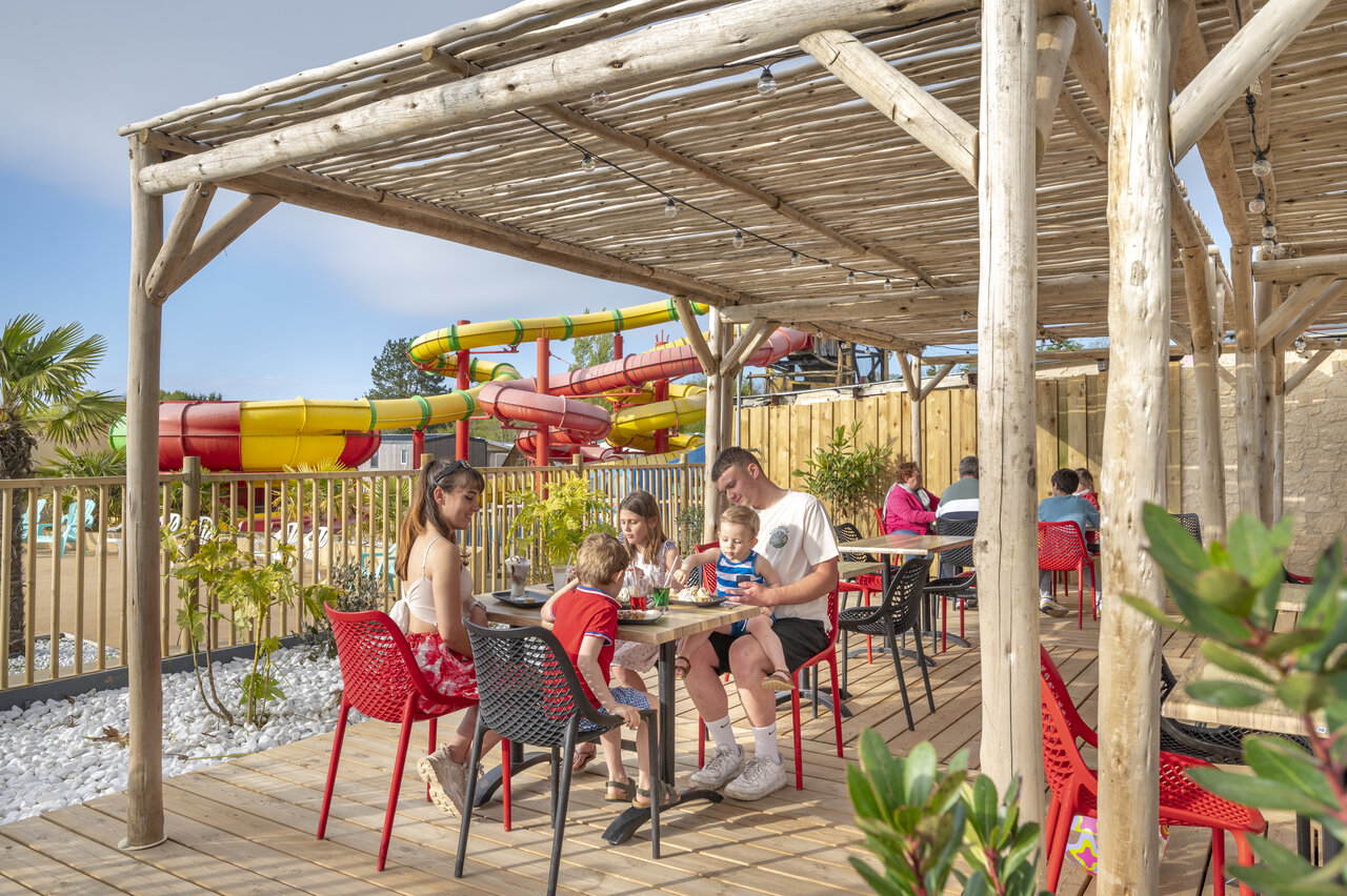 Family dining on restaurant terrace with water slides at CAPFUN Chateau d'Arvid campsite in Villerville (14).