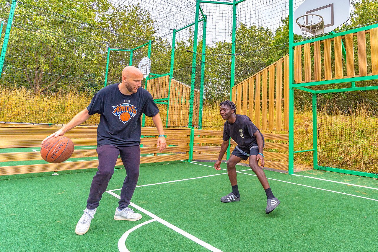 Two men playing basketball on multisport court at CAPFUN La Ch�naie campsite in PORNIC (44).
