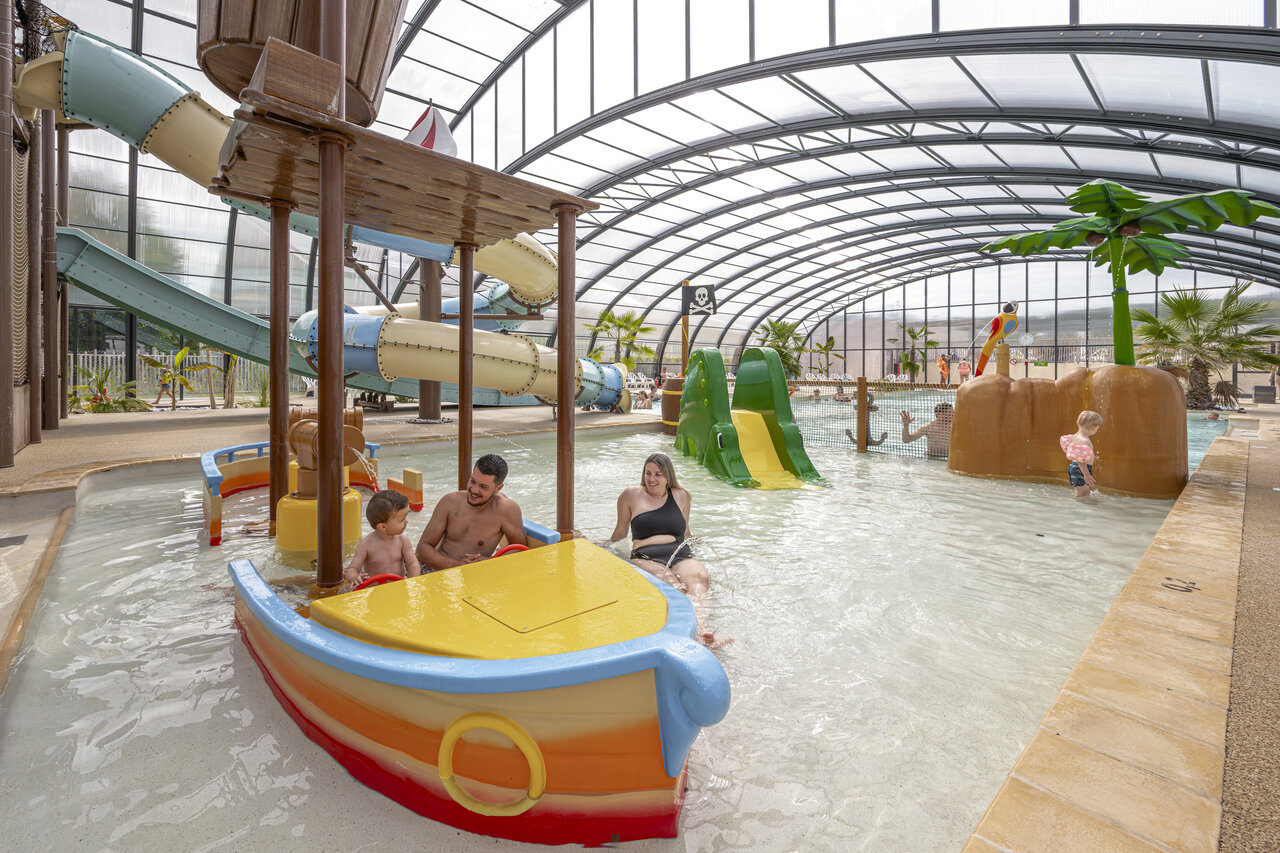 Indoor swimming pool with slides, pirate ship and water games at CLICOCHIC Chevaliers campsite in HOULGATE (14).