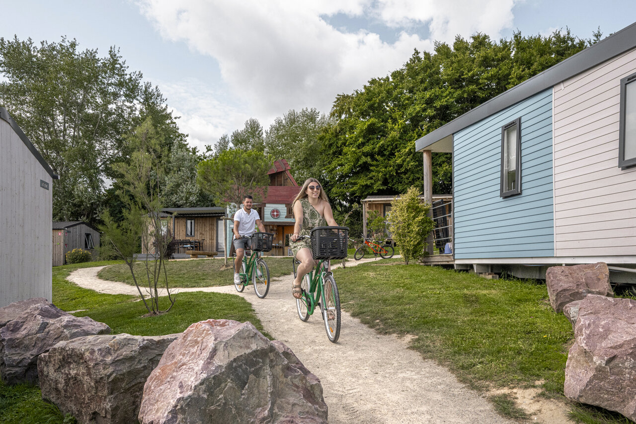 Couple cycling past mobile homes at CLICOCHIC Chevaliers campsite in HOULGATE (14).