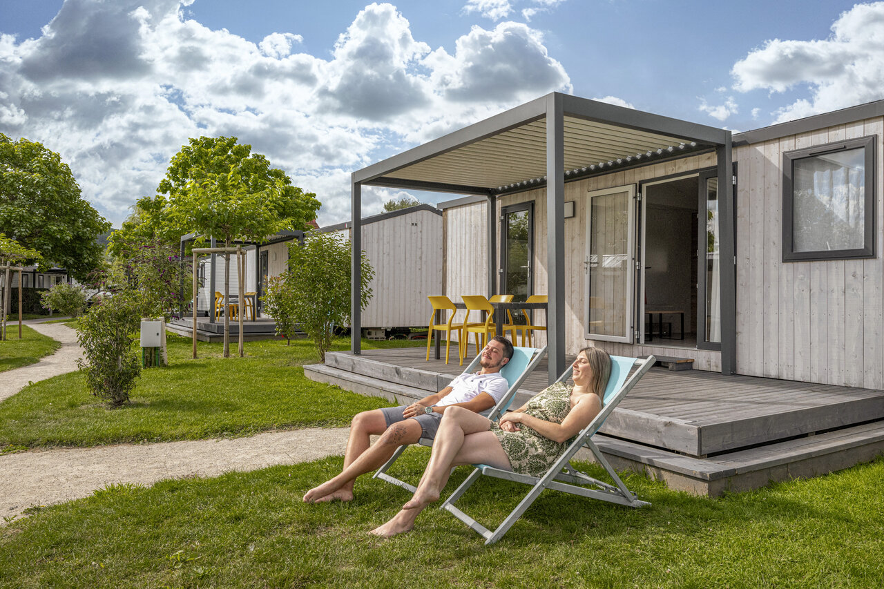 Modern mobile home with terrace, couple relaxing at CLICOCHIC Chevaliers campsite HOULGATE (14).