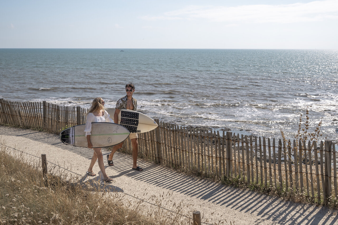 Surfers with boards on coastal path at CLICOCHIC Chouans campsite in Saint Hilaire de Riez.