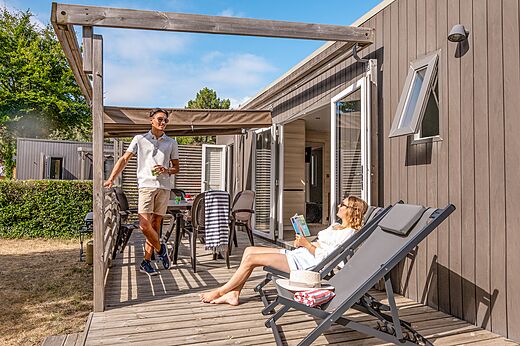 Modern mobile home with wooden terrace and couple at camping CLICOCHIC Chouans in SAINT HILAIRE DE RIEZ (85).