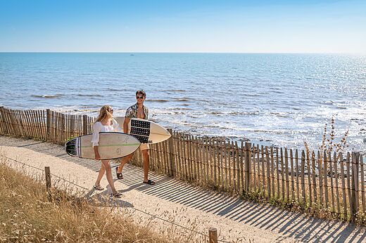 Couple with surfboards on path at camping CLICOCHIC Chouans in SAINT HILAIRE DE RIEZ (85).