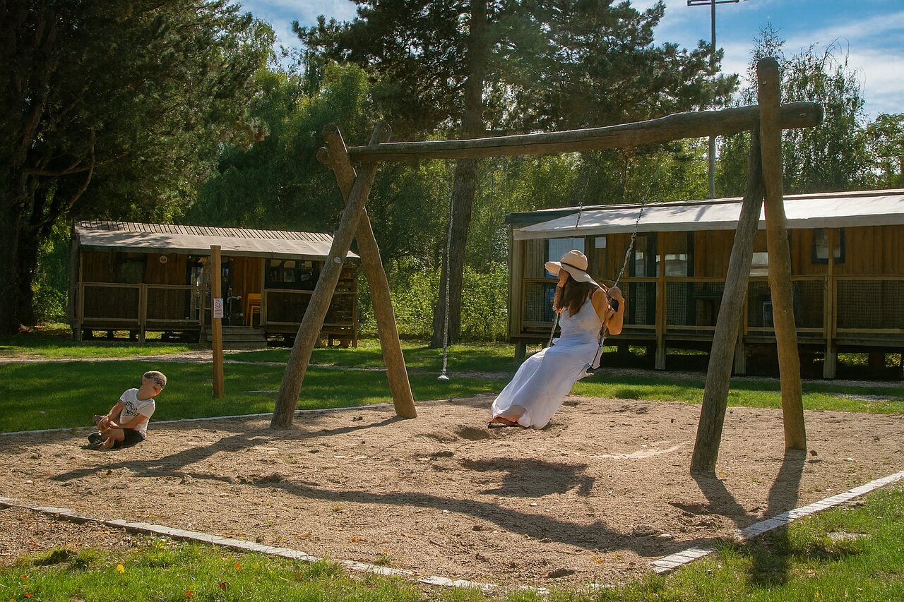Wooden swing, playground, and mobile homes at CLICOCHIC Au Clair Ruisseau campsite in Gerstheim (67).