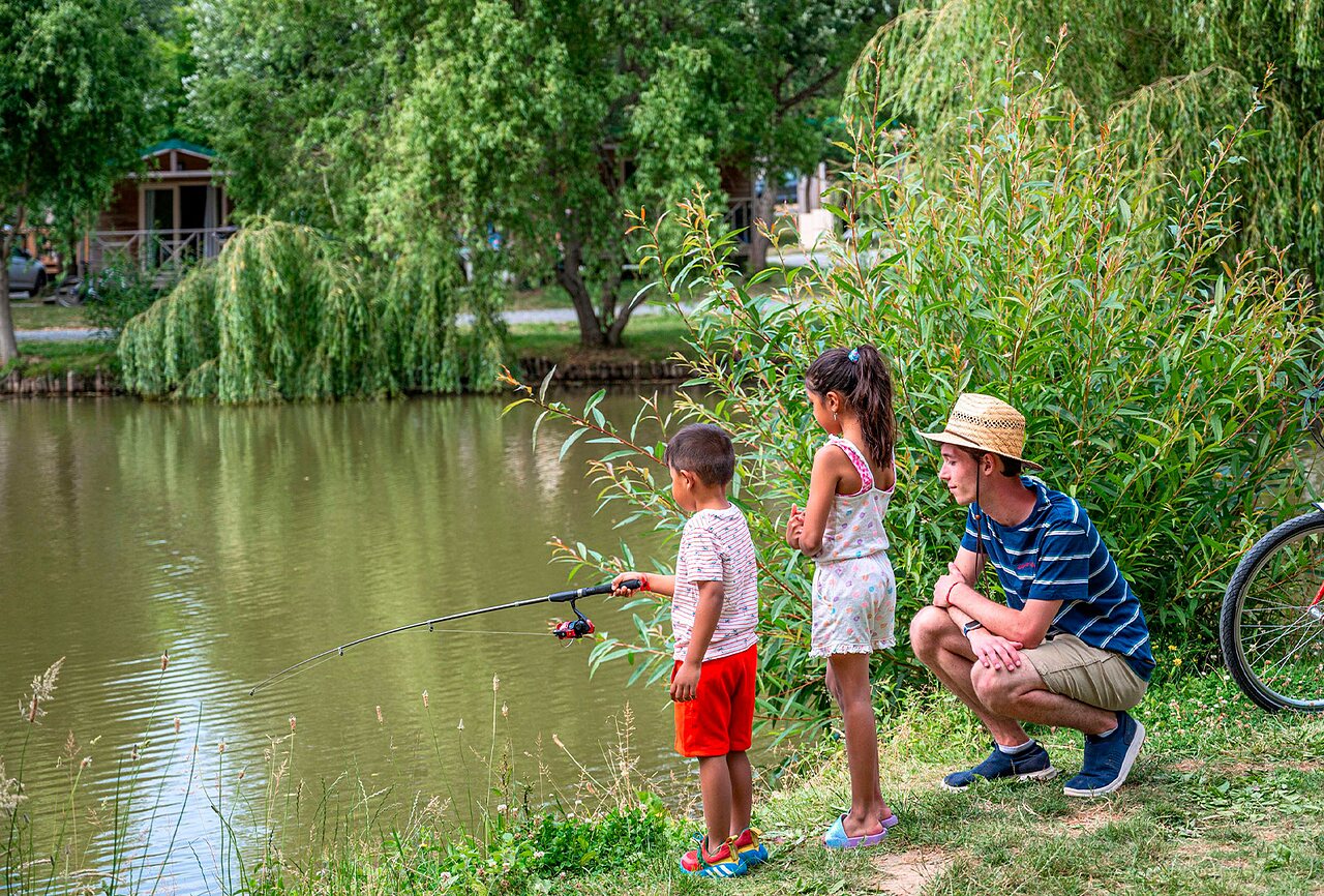 Children fishing by the natural pond at campsite CLICOCHIC Au Clair Ruisseau in Gerstheim (67).