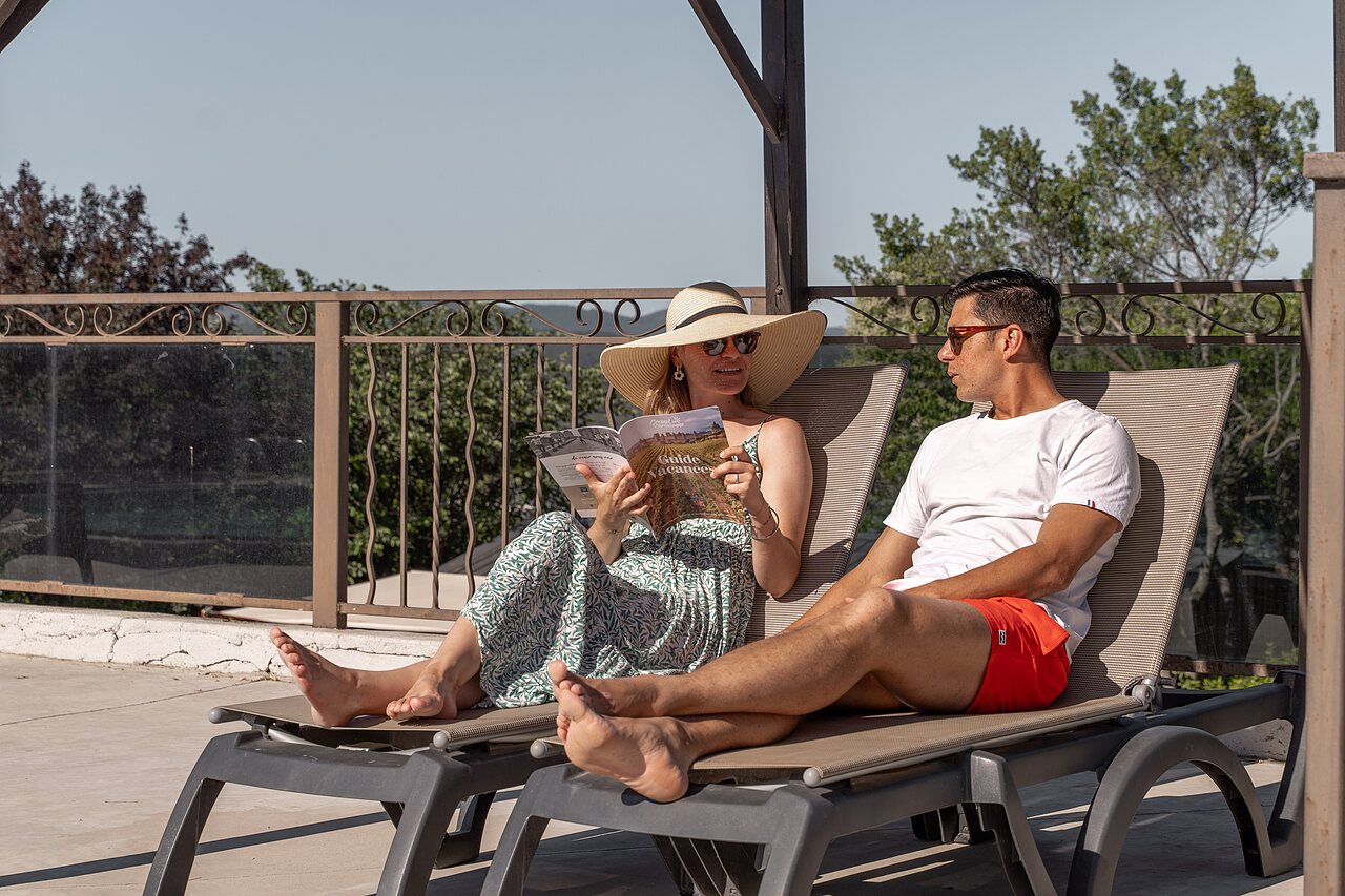 Couple relaxing on sun loungers on terrace at CLICOCHIC Commanderie campsite in Rustiques (11).
