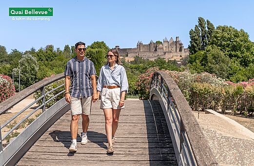 Couple walking on bridge, medieval city of Carcassonne in background, Aude.