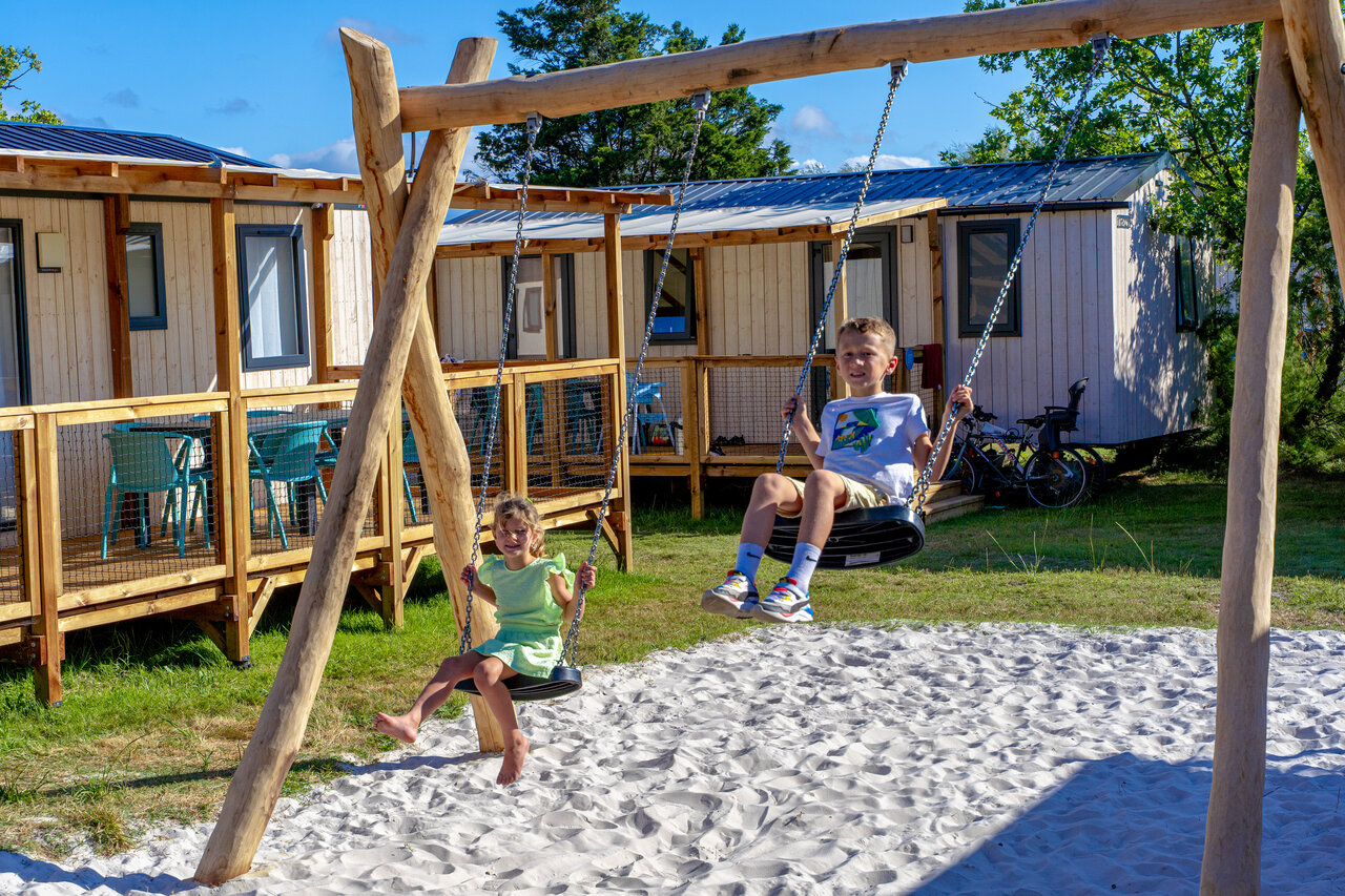 Children playing on wooden swing set in front of mobile homes at VAGUES OCEANES Coq Hardi campsite in Cassy-Lanton (33).