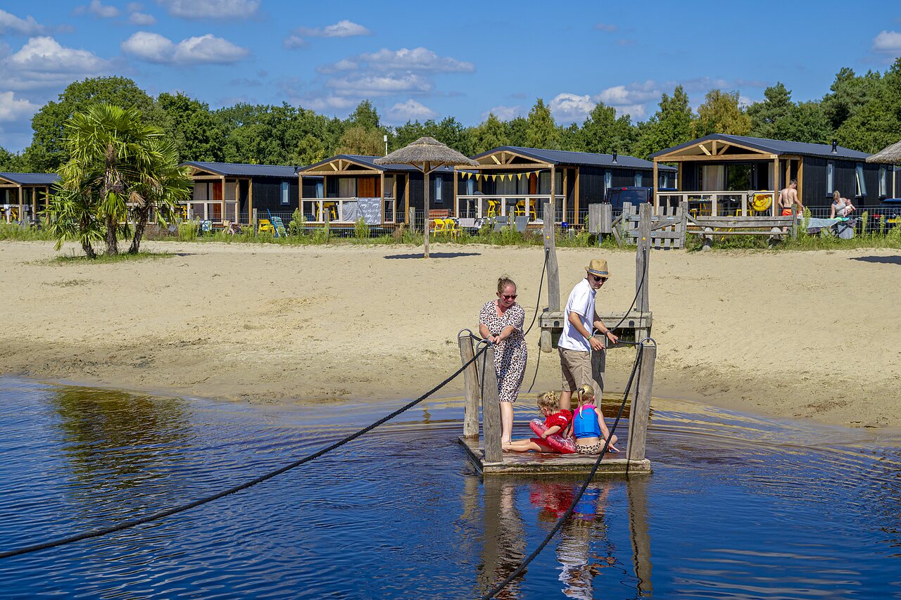 Family on raft, sandy beach and accommodations at CAPFUN De Belten campsite in Rheeze.