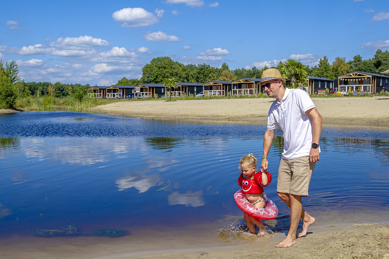 Father and child in the lake, beach and accommodations at CAPFUN De Belten campsite in Rheeze.