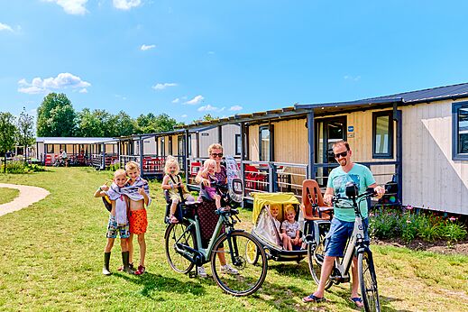 Family cycling in front of Mobile homes at CAPFUN De Eikenhof campsite.