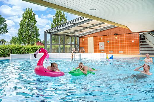 Indoor and outdoor swimming pool with family and inflatable toys at CAPFUN De Pekelinge campsite in Oostkapelle.