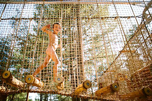 Naturist child playing on net play structure at LIBRANOO Naturiste Belezy campsite.
