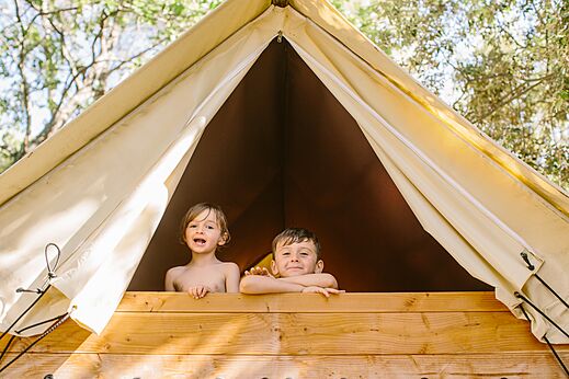 Smiling children in wooden glamping tent at LIBRANOO Naturiste Belezy in Bédoin (84).
