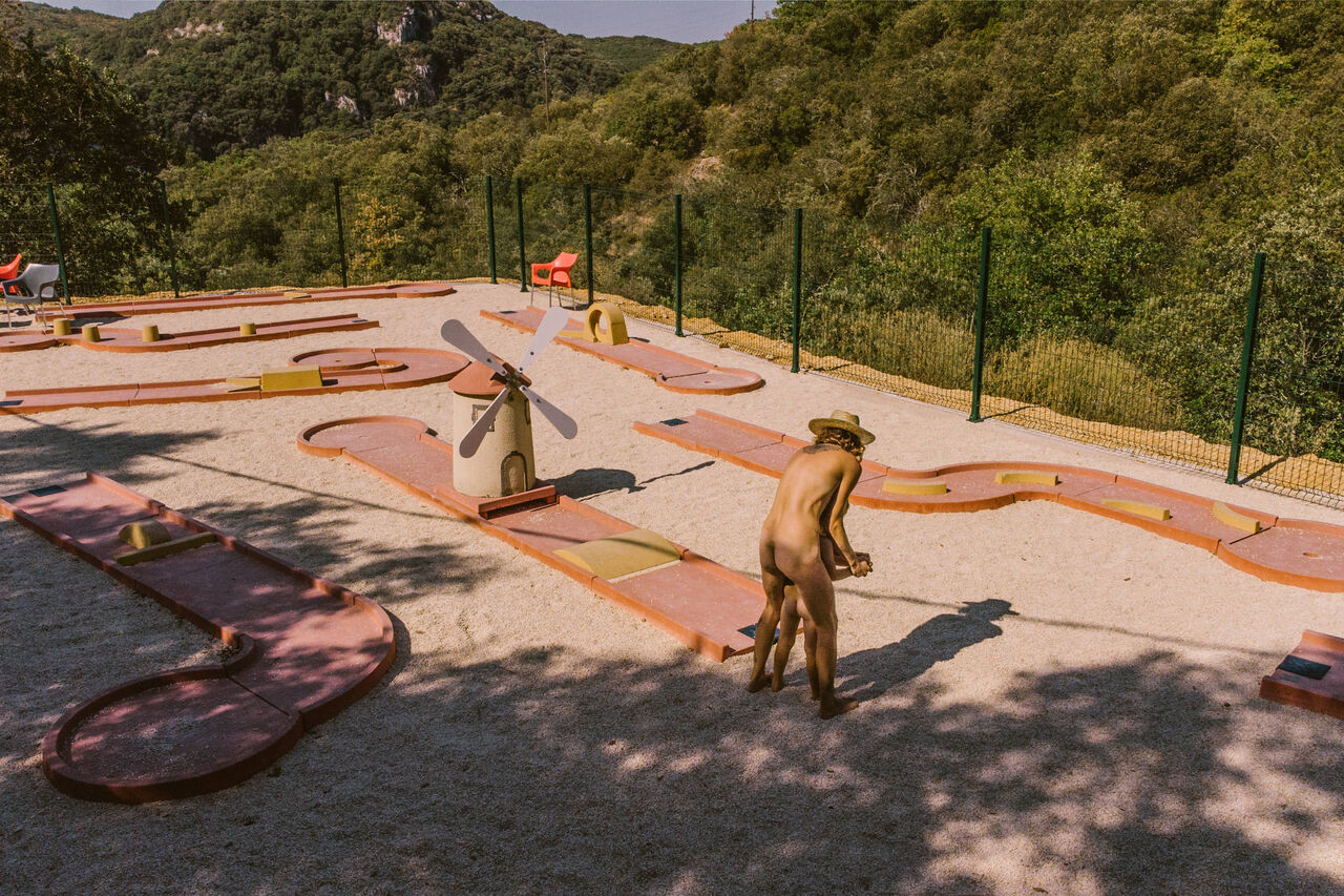 Mini-golf course with windmill, naturist person playing at LIBRANOO Naturiste Sabliere campsite in Barjac (30).